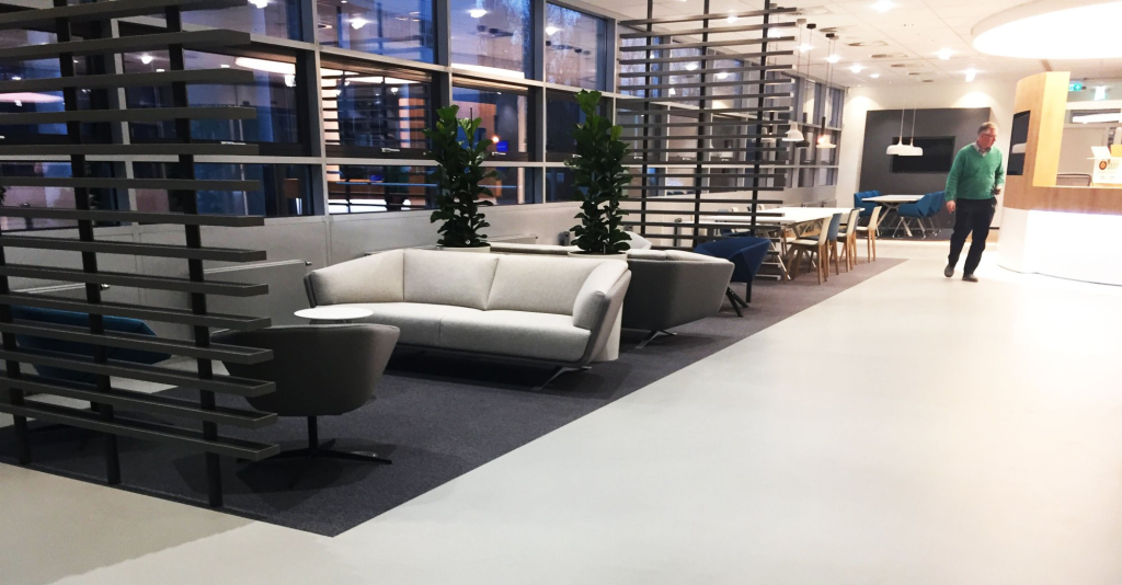 Lichtgrijze gietvloer in een kantoorlounge met zithoek en houten roomdivider