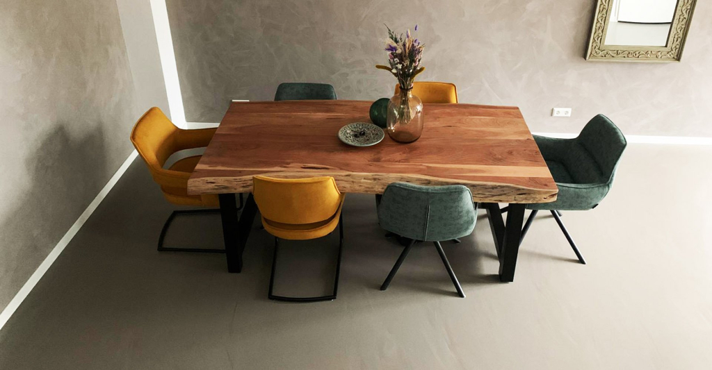 Grijsbruine gietvloer in een eetkamer met houten boomstamtafel en okergele stoelen