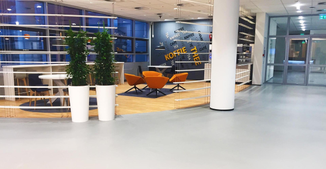 Lichtgrijze coatingvloer in een kantoorkoffiehoek met oranje fauteuils