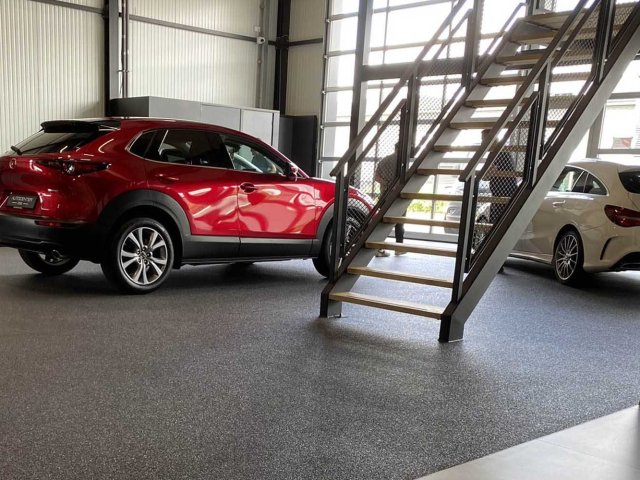 Grijze grindvloer in een autoshowroom met rode Mazda en stalen trap
