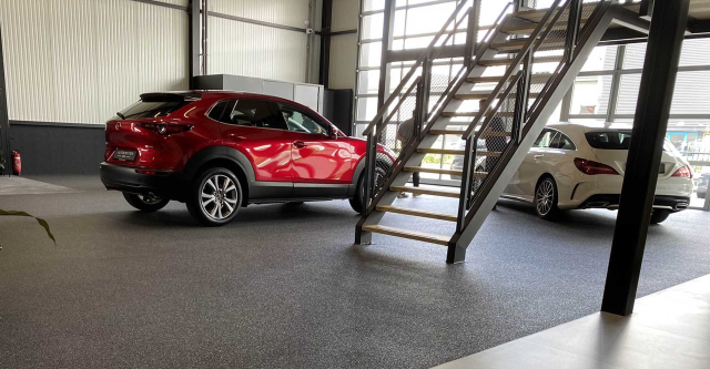Grijze grindvloer in een autoshowroom met rode Mazda en stalen trap