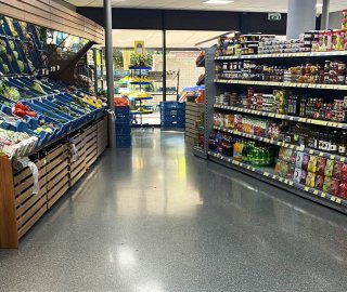 Grijze mortelvloer met grindstructuur in een supermarkt tussen de schappen