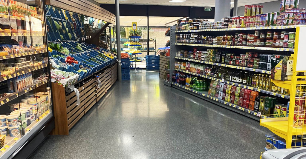 Grijze mortelvloer met grindstructuur in een supermarkt tussen de schappen