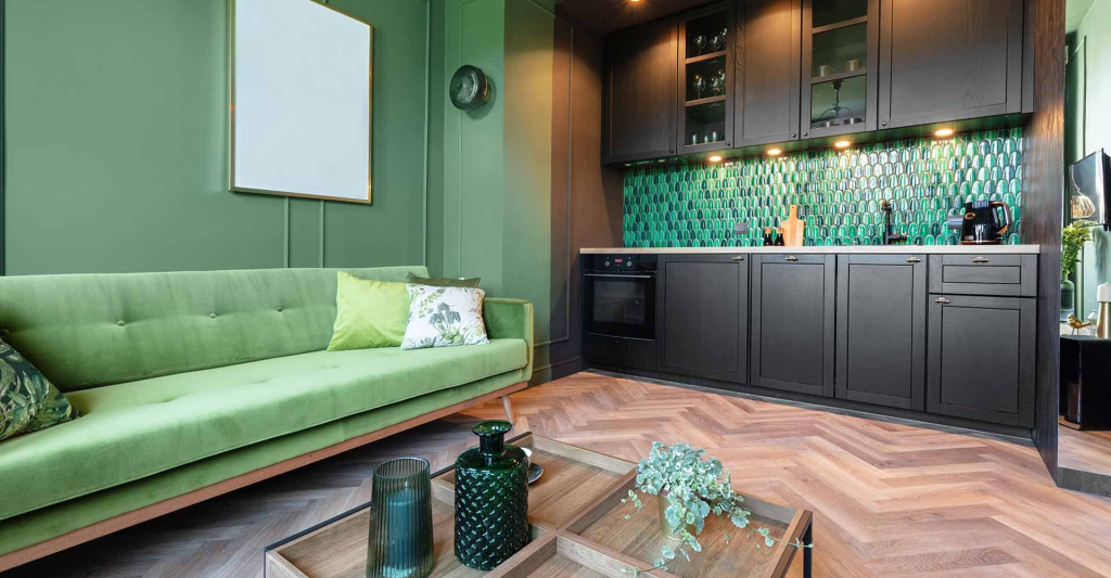 PVC vloer in visgraatmotief in een woonkamer met groene bank en donkere keuken